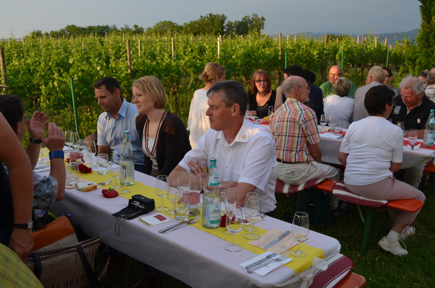 An langen, festlich eingedeckten Tischen sitzen zahlreiche Menschen zusammen und genießen eine Weinprobe bei guter Stimmung.
