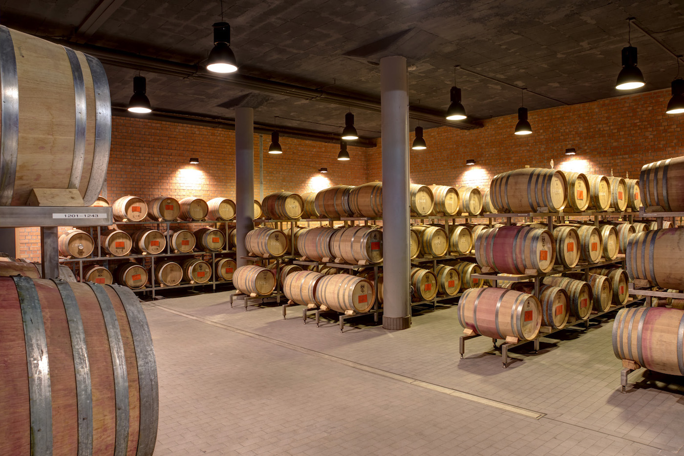 Blick in einen moderneren Weinkeller, in dem in Reihen aufgestelle größere und kleinere Weinfässer aus Holz lagern.